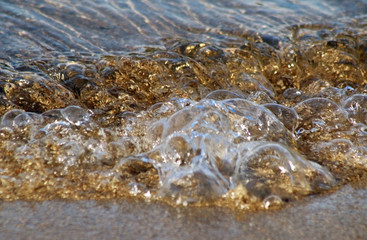 Soft rolling wave of gold in soft focus moving across tiny pebbles at shoreline