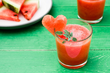 Fresh watermelon blended drink with mint leaves and a heart of watermelon in glasses and slices of watermelon on a wooden table
