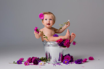 baby girl 1 year old sitting in a bucket of flowers on a light background. space for text