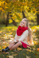 Happy pretty blonde teen girl is wearing fashion red scarf walking in autumn park with yellow leaves