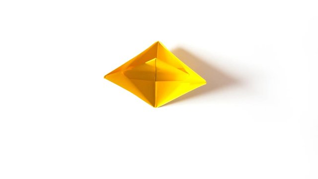Yellow paper origami boat folding and unfolding itself, then sailing away. Creative loopable 4K stop motion timelapse, top view, white background.