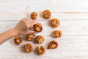 Woman's hand holding a Pepperoni Roll. Red sauce and rolls in the form of a spiral on a white wooden background. Tasty italian fast food