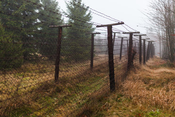 Barbwire fence. Part of the czech german borderline in the middle of a foest on a grey and foggy autumn morning.