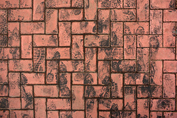 Grunge background. Many black asphalt draggled footprints on red stone block pavement/ bricks. Vertical direction of footprints