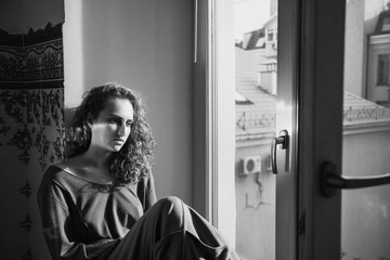 Beautiful young sad girl is sitting by the window