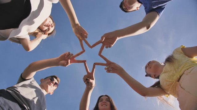 Friends make a star shape from their hands against a blue sky
