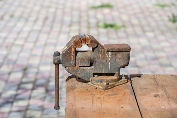 Old rusty vise for metal products on wooden table, outdoors, close up