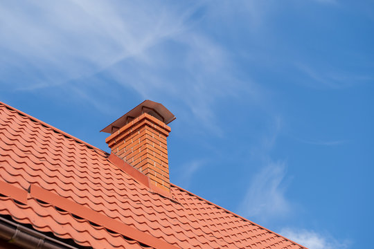 Red roof of a detached house and chimney against the blue sky, closeup
