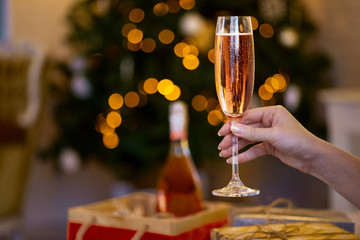 Female hand holding glass of champagne, party celebration. Holidays, people and celebration concept. Christmas tree in the background