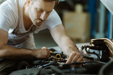 Close up of young auto mechanic examining engine in a workshop