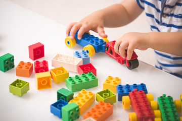 Toddler child playing multi-colored cubes on the table. Colorful plastic bricks for the early...