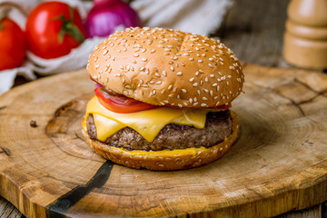 Burger with meat and cheese and tomatoes on wooden board