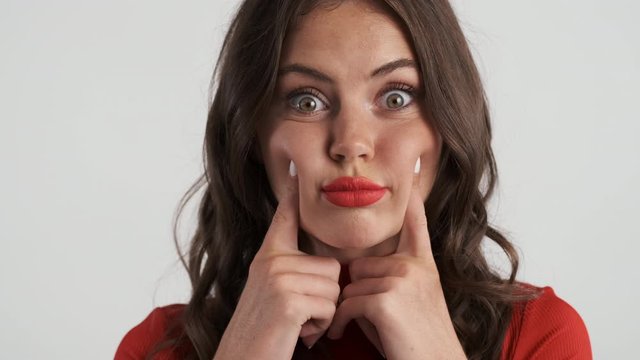 Portrait of attractive brunette girl puffing out her cheeks on camera over gray background