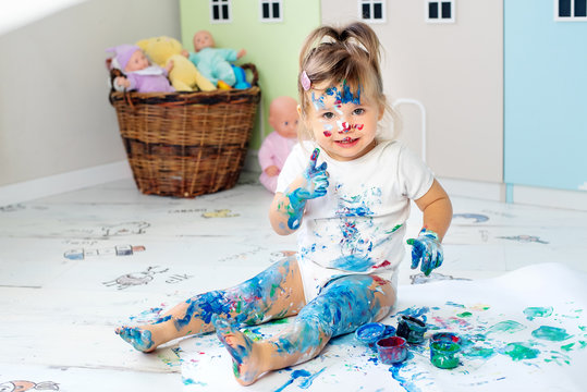 Little cute girl draws with finger paints on the floor. Early development concept