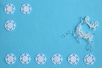 Fototapeta na wymiar Christmas white decorations deer and felt snowflakes on blue fabric background. Flat lay. Christmas and New Year frame