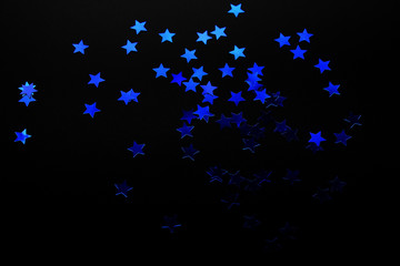 Blue shiny star shape confetti on black background. Gradient from really dark to light stars. Copy space