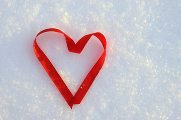 Red satin ribbon in form of heart on the snow. Romantic background. Copy space
