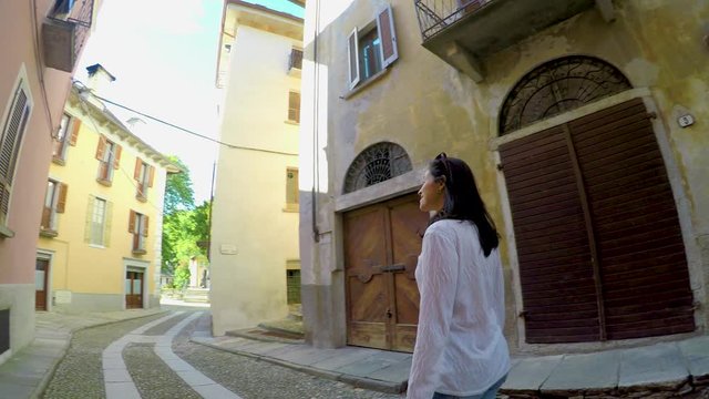 Woman Walking Down Old Street In Vogogna, Italy. Female Traveler Looking Around and exploring