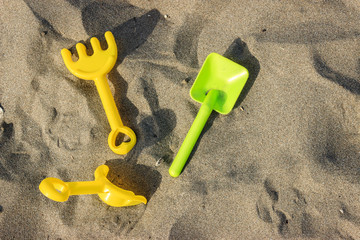 Plastic toy yellow and green shovels on beach sand in summer day. Summer vacation concept