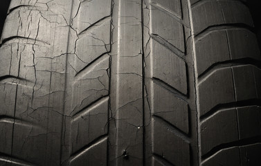 Old black tire with worn tread and cracks, worn old car tire tread, old damaged, worn black tire tread, large cracks in the car wheel, tire black color for background.
