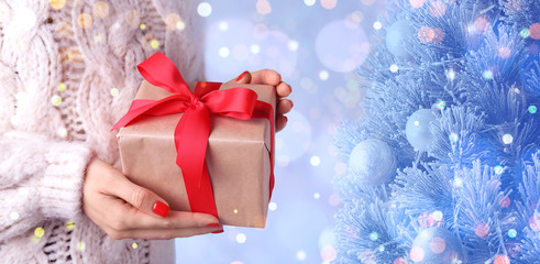 Young woman with gift near Christmas tree, closeup. Bokeh effect