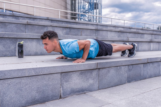 male athlete, tanned man, summer city, push-ups, lying on bench, chest training, bar on press, bottle protein with water, fitness workout, background concrete steps. Free space for motivation text.