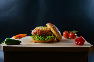 An appetizing hamburger on a wooden board with fresh vegetables.