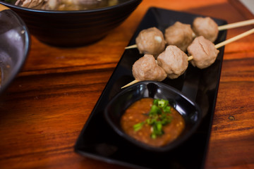 Grilled meatballs placed on a black plate with dipping sauce on wood background