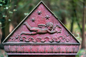 Triangular part of a tombstone showing a flying cherub on red background