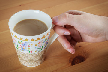 Young caucasian man hand holding coffee with milk in patterned mug on wooden table  background  