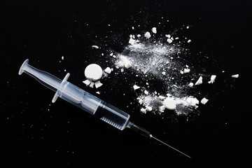 Syringe and crushed white pills on black background. Top view