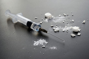 Syringe and crushed white pills on black background. Selective focus
