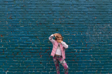 girl stands and makes signs with hands near a blue wall