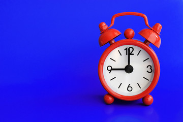 Cute red metal alarm clock on dark blue background. Nine o'clock. Copy space