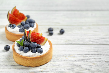 Tarts with blueberries and figs on white wooden table, space for text. Delicious pastries