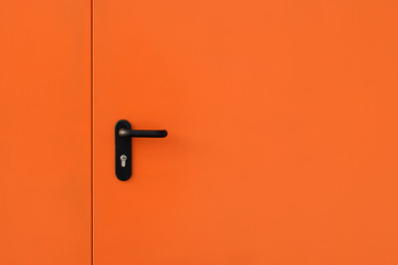Orange modern metal door with black metal handle and turned keyhole. Copy space
