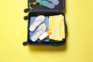Open suitcase and beach accessories on yellow background, top view