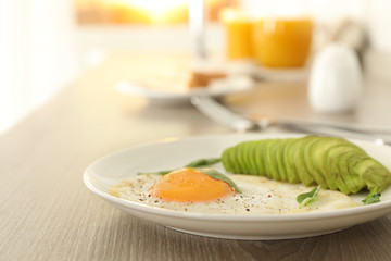 Tasty breakfast with fried egg and avocado on wooden table, closeup