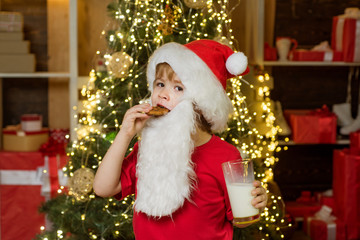 Fototapeta na wymiar Happy Santa Claus - little child boy with glass of milk and cookie. Portrait of surprised and funny Santa. Cookies for kids Santa Claus. Santa Claus. Christmas child.