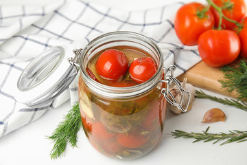 Pickled tomatoes in glass jar and products on white table