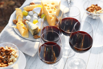 Red wine and snacks served for picnic on white wooden table outdoors