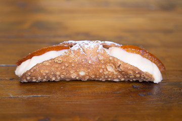 Dulce típico de Palermo, Italia: cannolo Vista lateral de un cannolo de naranja. Se ve la parte de fuera crujiente y la crema del interior con su adorno de naranja. Reposa sobre una mesa de madera