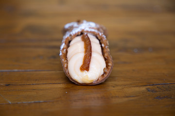 Dulce típico de Palermo, Italia: cannolo Vista frontal de un cannolo de naranja. Se ve la parte de fuera crujiente y la crema del interior con su adorno de naranja. Está sobre una mesa de madera 