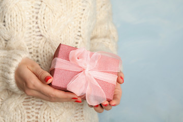 Young woman holding Christmas gift on blue background, closeup