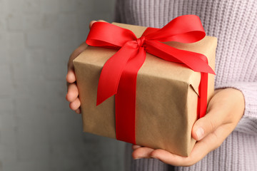 Young woman holding Christmas gift on light background, closeup