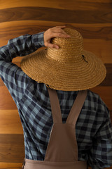 the woman wearing county style clothes and wicker hat stands in front of wooden wall.