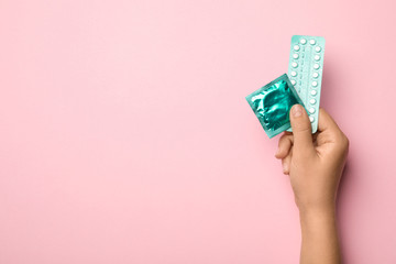 Woman holding condom and birth control pills on pink background, top view with space for text. Safe...