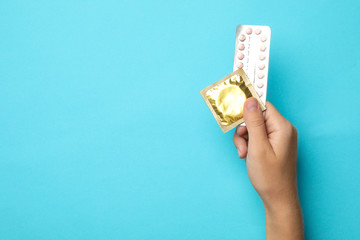 Woman holding condom and birth control pills on blue background, top view with space for text. Safe...