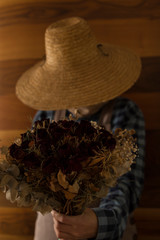 the woman wearing county style clothes and wicker hat stands in front of wooden wall.