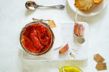 Sun-dried tomato with oil and garlic in the glass on wood board and the white background. Copy space.
